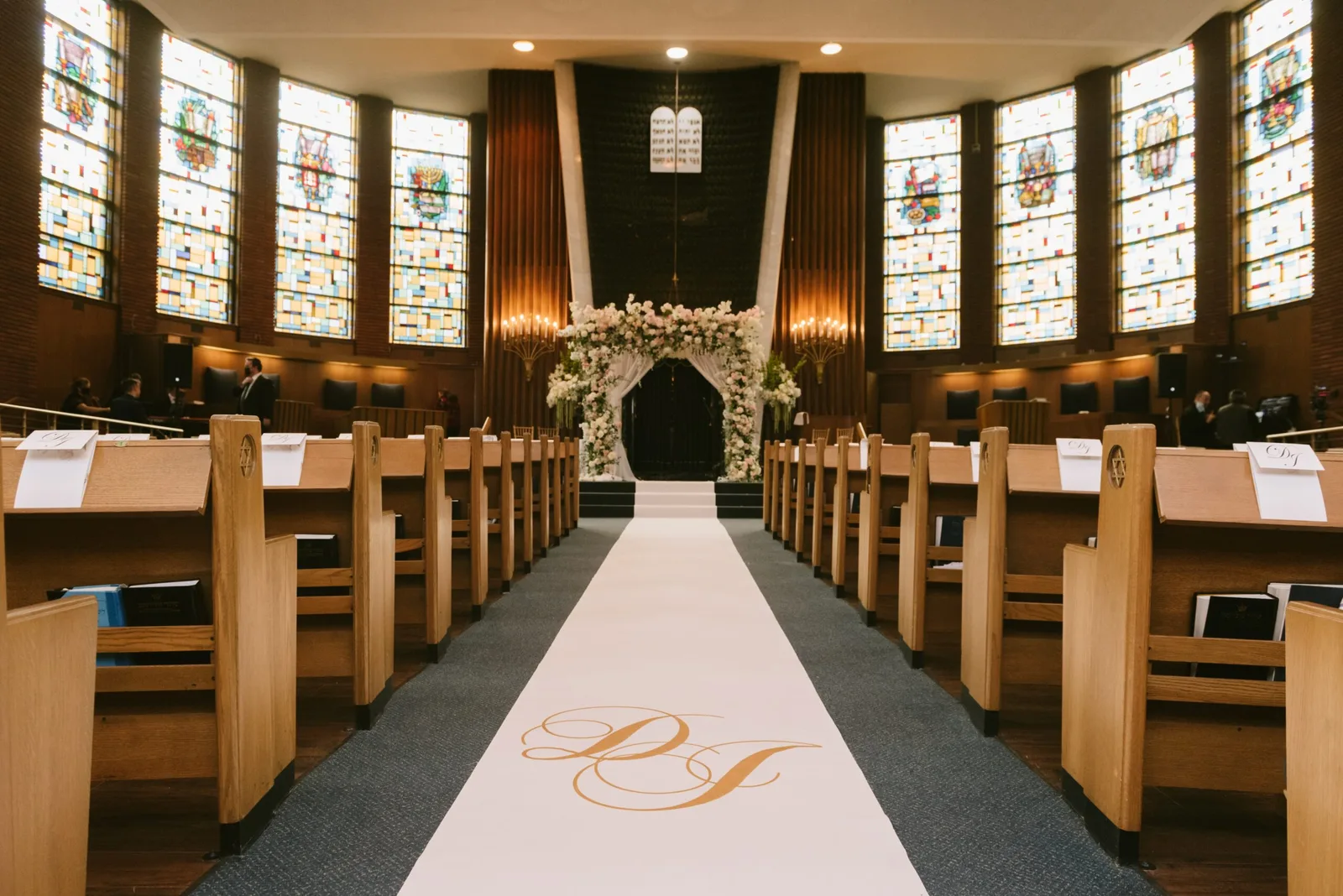 Sanctuary with stained-glass windows and a monogrammed white aisle runner