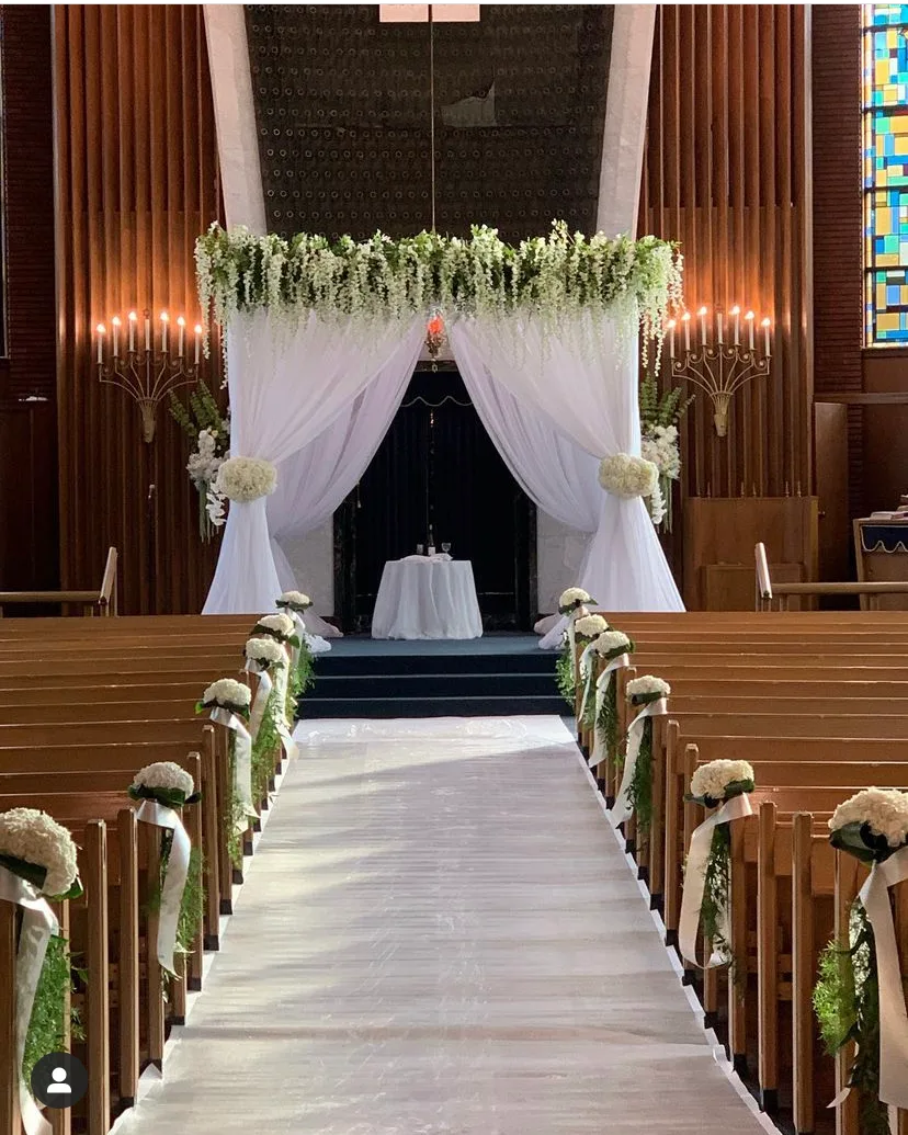 Sanctuary aisle lined with flowers leading to a white draped wedding canopy