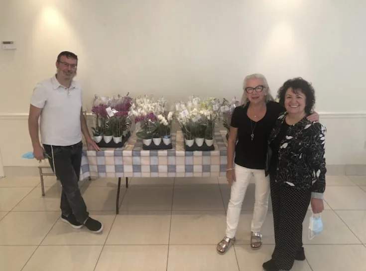 Three people standing by a table of potted orchids