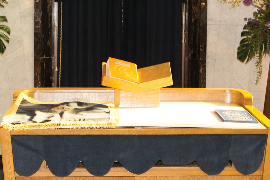 Bimah table draped in dark cloth with an open golden book stand and a prayer shawl