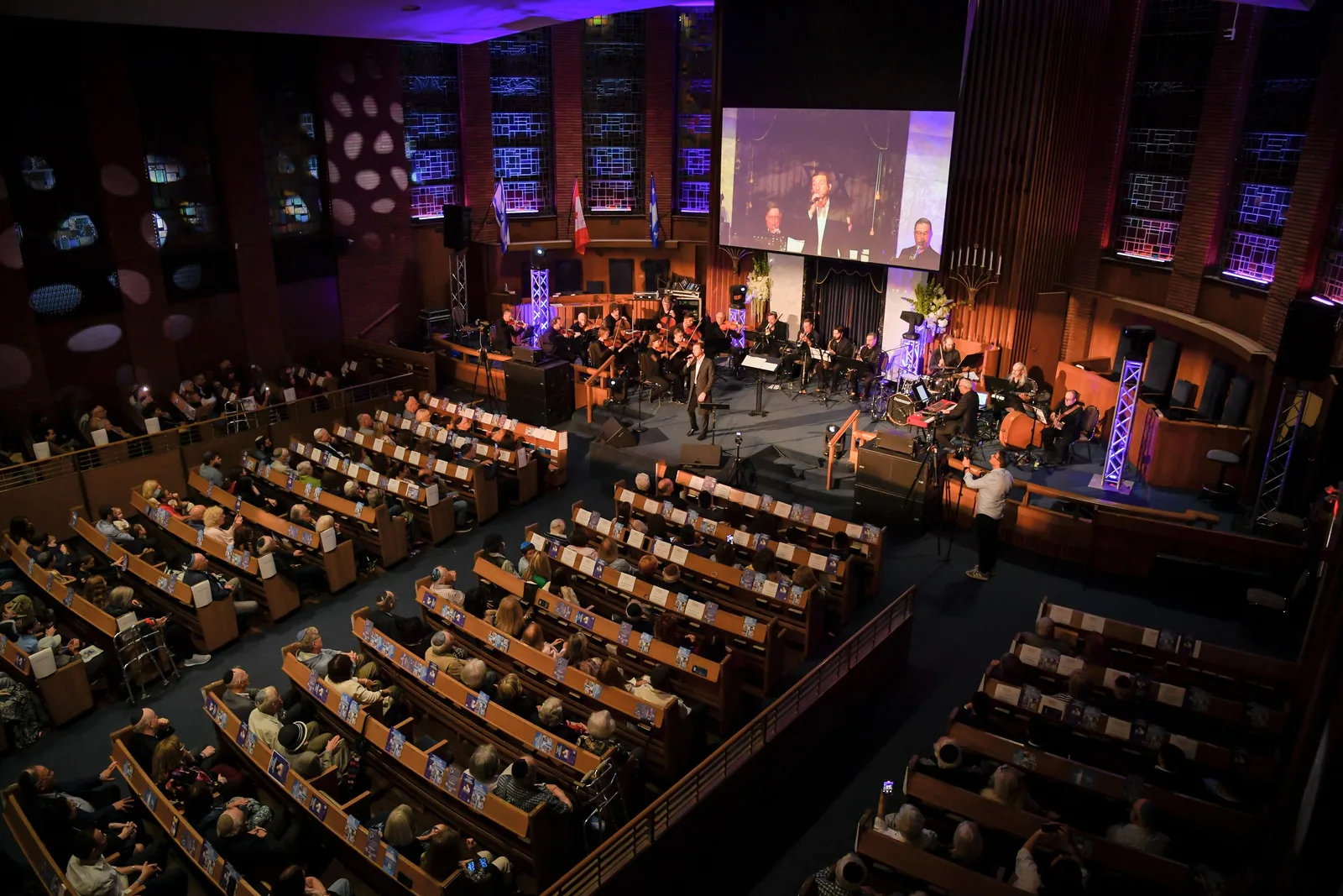The sanctuary from the balcony during an evening concert: full pews, an orchestra on the stage and tall stained-glass windows lit blue