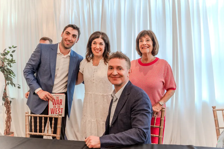 A young man holding a copy of The War on the West poses with two women and a seated author