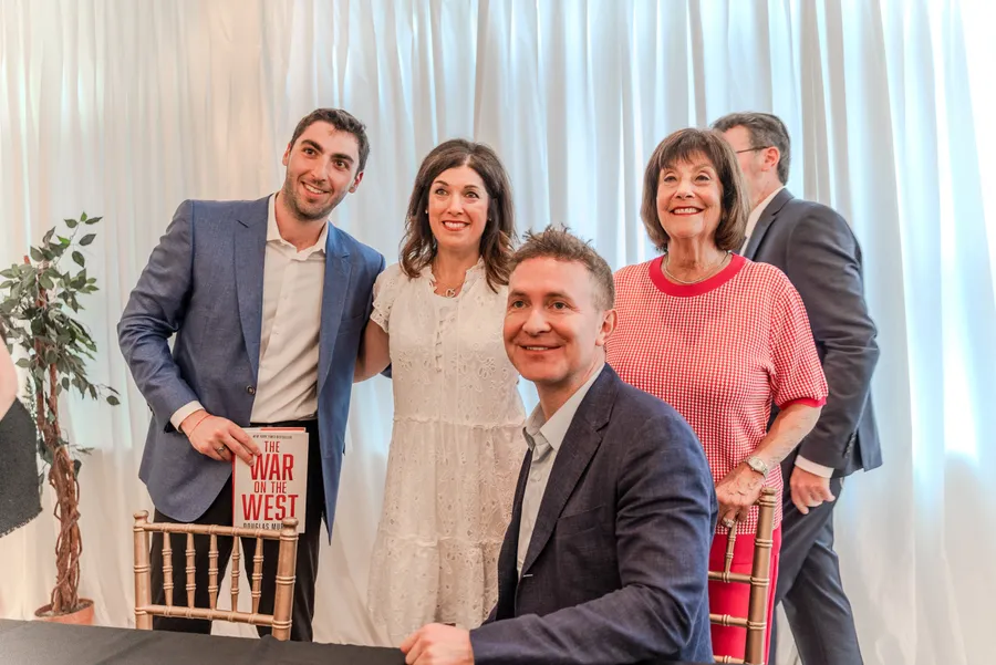 A young man holding The War on the West poses with two women and a seated author