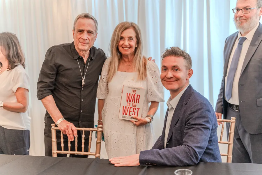 A man and a woman holding The War on the West pose with a seated author at a signing table