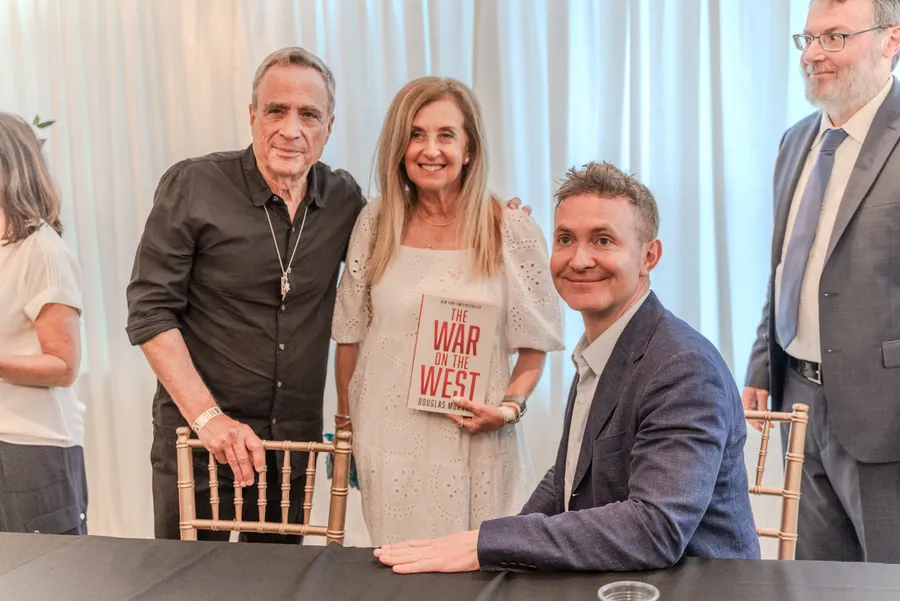 A couple poses with a seated author, the woman holding the book The War on the West