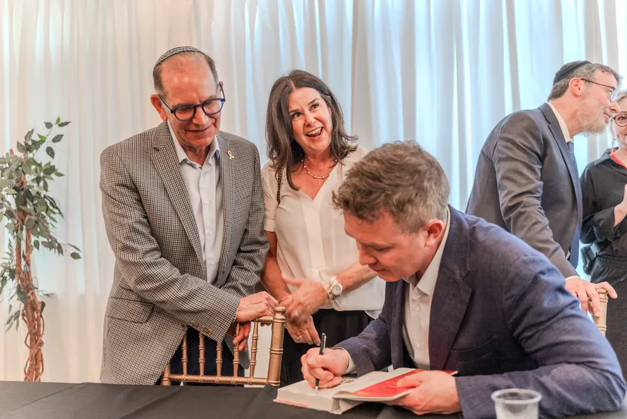 A seated author signs a book while a smiling couple stands beside the table