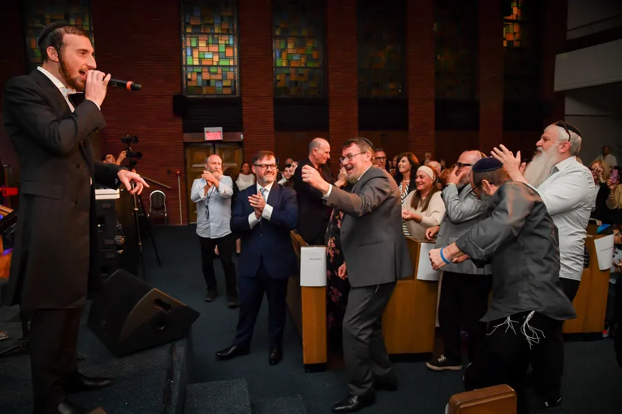 The singer leads the crowd from the steps of the stage as men dance in the aisle, the stained-glass windows behind