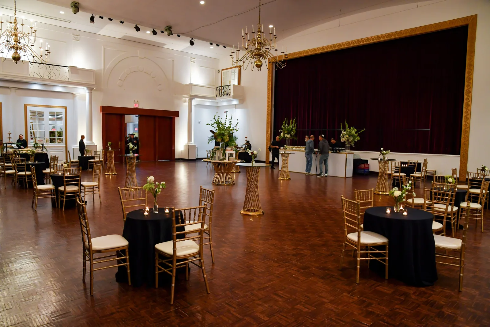 Singerman Hall: crystal chandeliers, the stage with its red curtain, and cocktail tables on the parquet floor