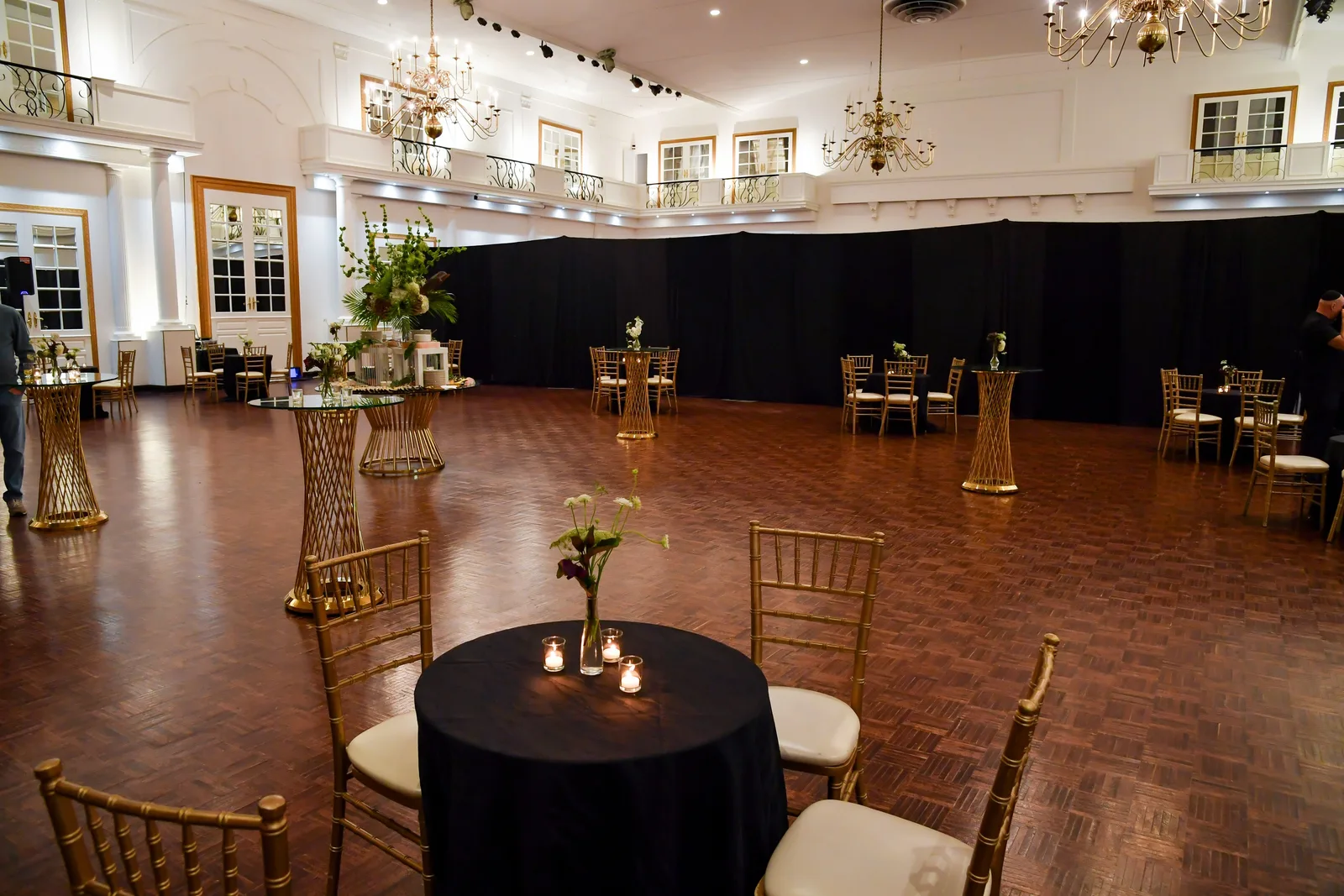 Singerman Hall’s open parquet floor with gold chairs, tall tables and chandeliers, under the balconies