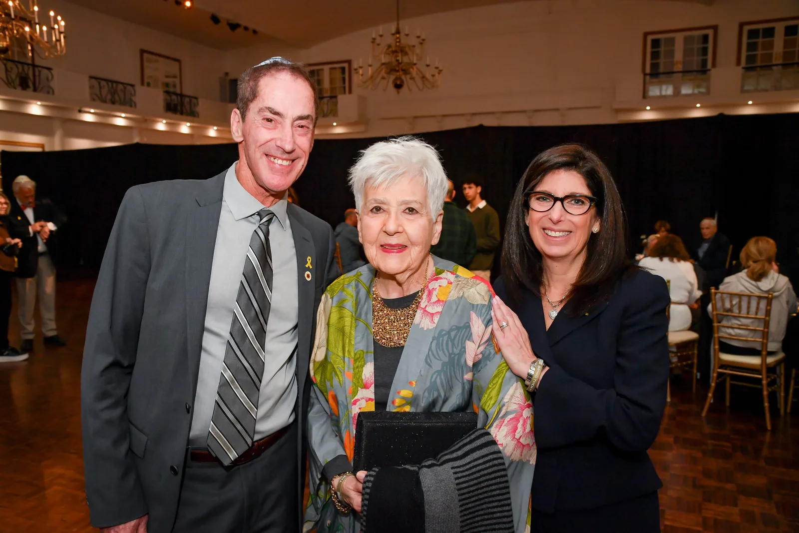 Three smiling guests under a chandelier in Singerman Hall