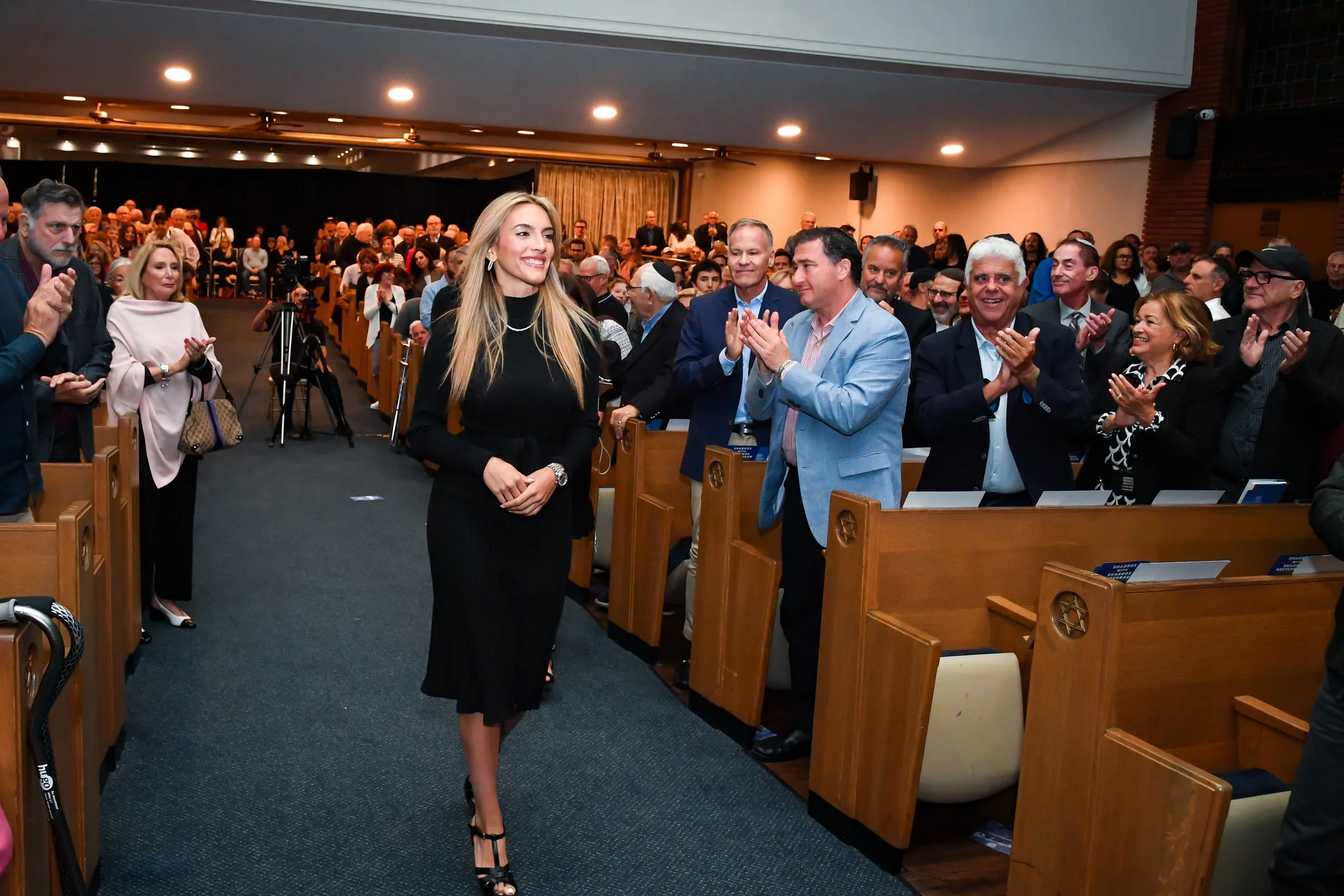 Emily Austin walking down the centre aisle, the audience standing and applauding on both sides