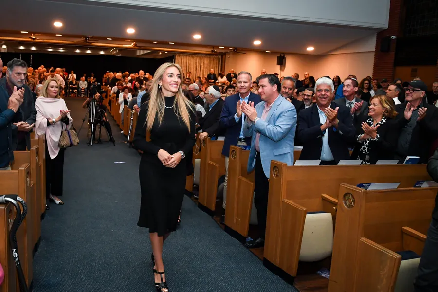 Emily Austin walking down the centre aisle, the audience standing and applauding on both sides