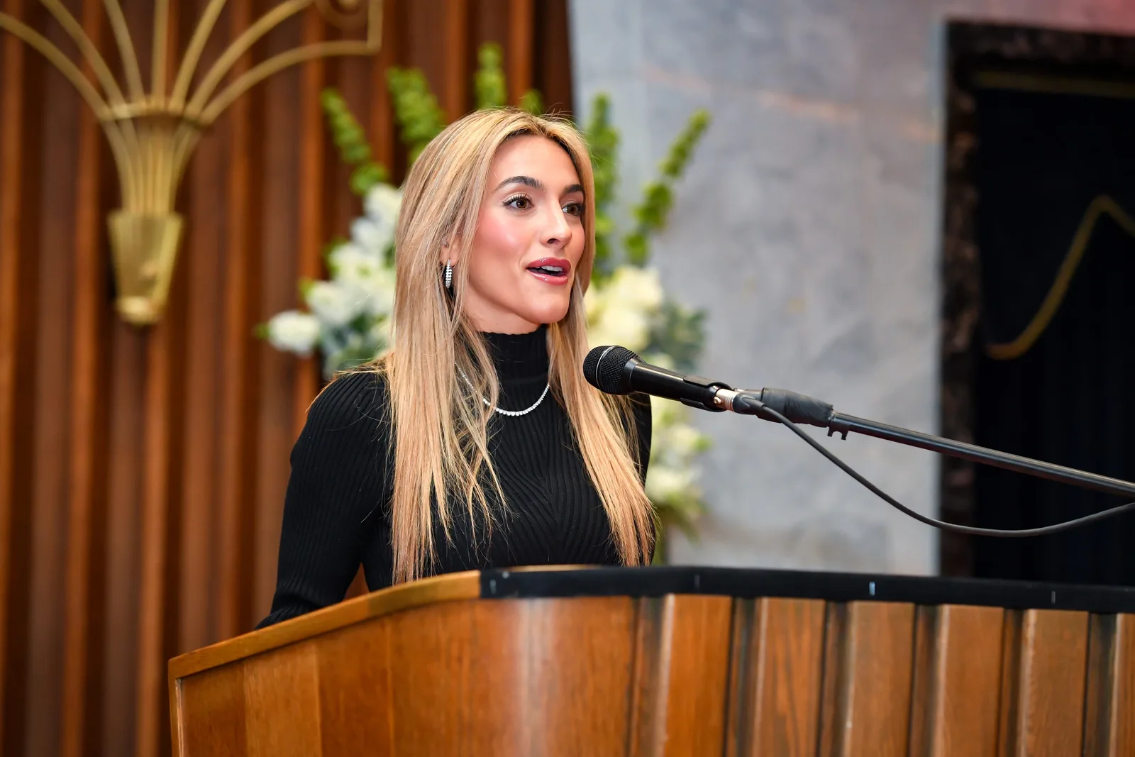 Emily Austin speaking at the lectern, flowers and the ark’s marble frame behind her