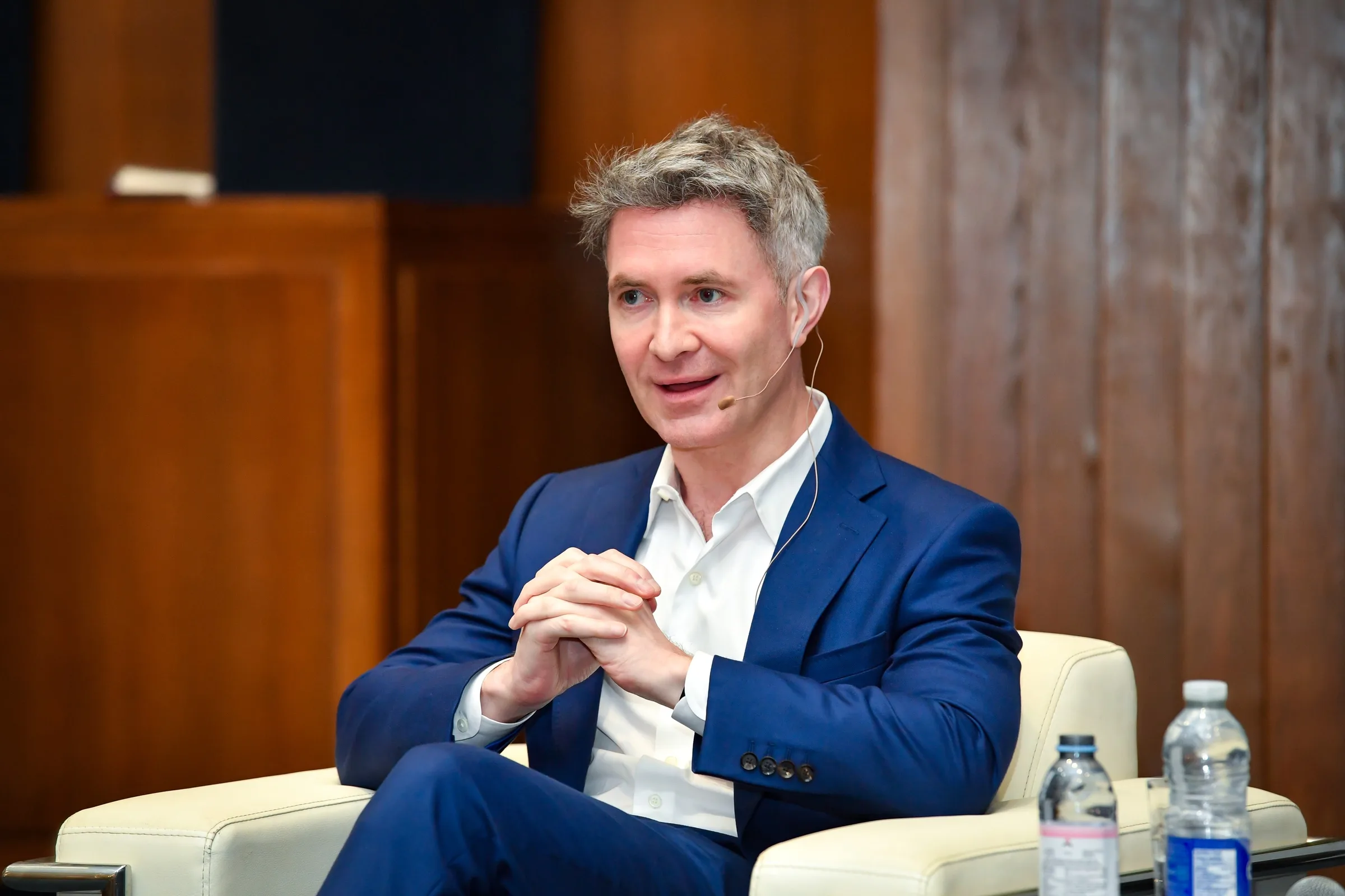Douglas Murray, in a blue suit, speaking from a white armchair