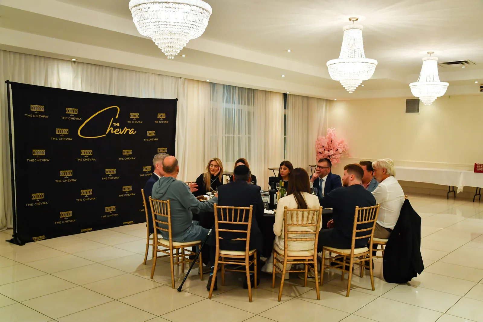 A dinner at a round table in the white hall with crystal chandeliers, tiled floor and sheer curtains
