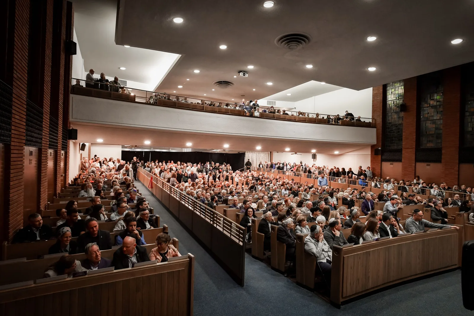 A full house in the sanctuary, seen from the side: every pew taken, the balcony filled above, in warm evening light