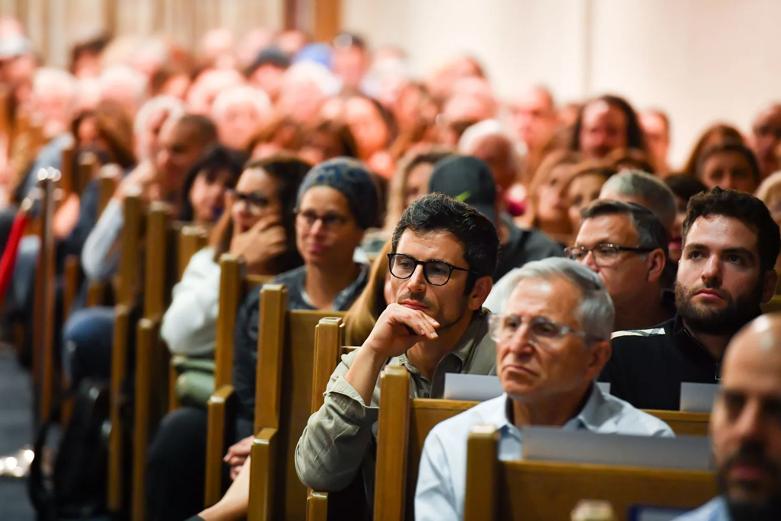 A man in glasses listening in the sanctuary pews, deep in thought, his chin resting on his hand, an older man beside him