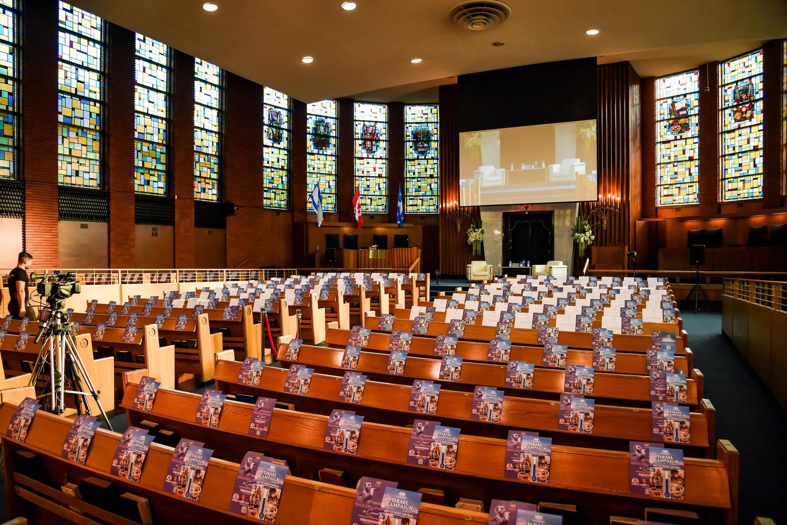 The whole sanctuary in daylight: tall stained-glass windows on both sides and rows of wooden pews set with programmes