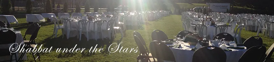 Tables set on the grass in Hampstead Park at dusk: the shul’s Shabbat Under the Stars banner